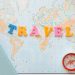 Flat lay of a map with colorful letters "TRAVEL" and a compass for planning adventures.
